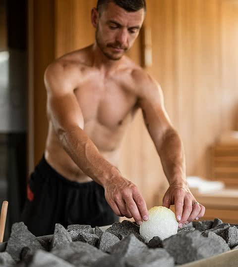 Junger Mann mit Bart bei den letzten Vorbereitungen für einen Saunaaufguss im Wellnesshotel Sonnen Resort in Südtirol.