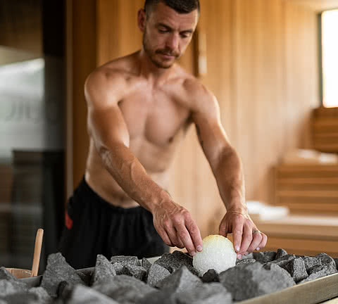 Junger Mann mit Bart bei den letzten Vorbereitungen für einen Saunaaufguss im Wellnesshotel Sonnen Resort in Südtirol.