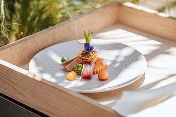 Gourmeturlaub Ein kunstvoll angerichteter Teller mit frischem Fisch, buntem Gemüse und einer essbaren Blüte im Design Hotel Sonnen Resort Naturns.