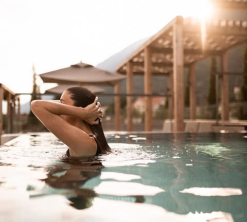 Junge Frau beim Auftauchen aus dem Wasser des Infinity-Rooftop-Pools im Wellnesshotel Sonnen Resorts Südtirol